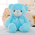 Large blue teddy bear plush toy with bow sitting on a bed in a cozy bedroom setting